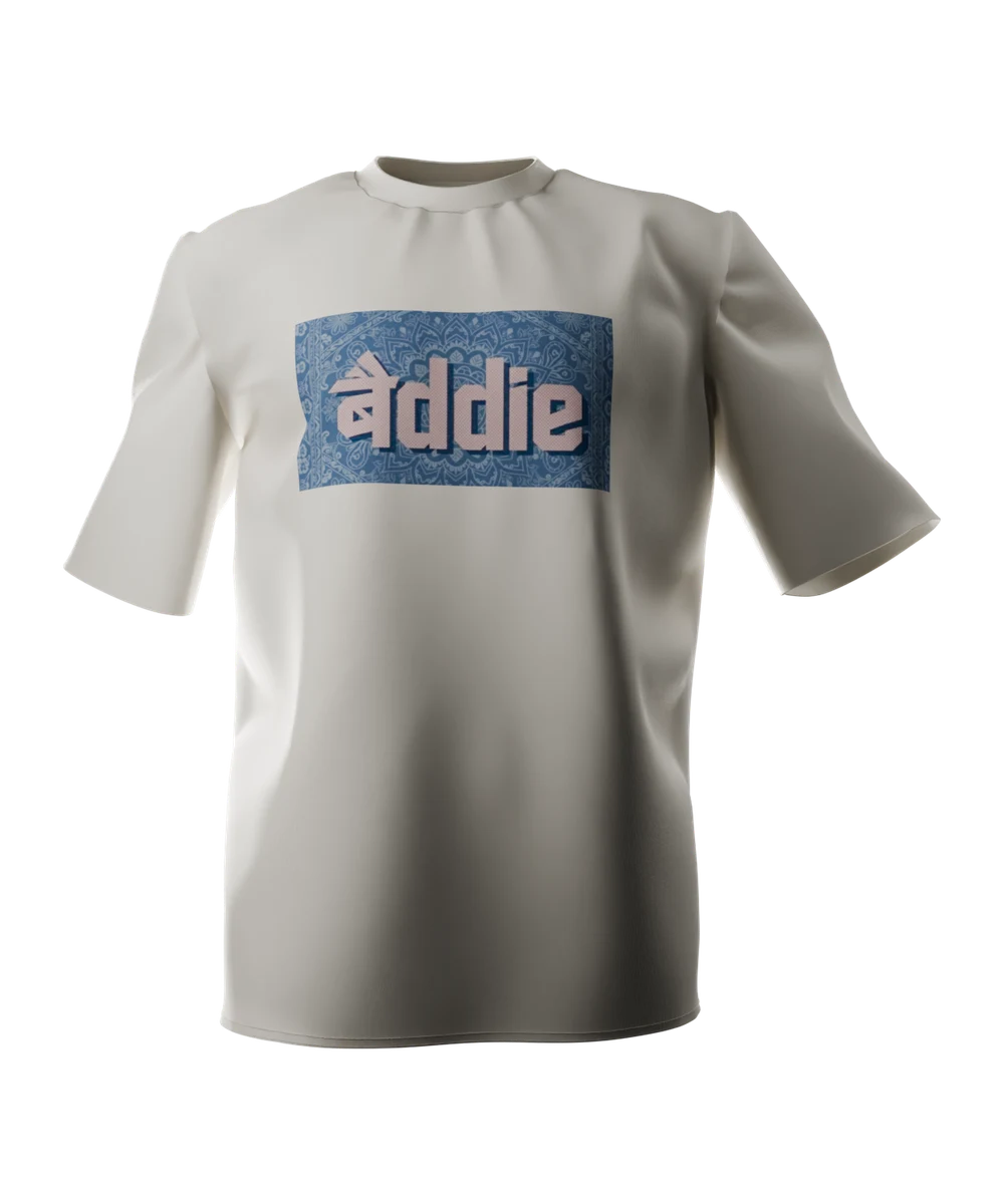 Bone t-shirt seen from the front, printed across the chest with the word baddie, its first syllable in Devanagari, in dusty pink halftone on a blue paisley ground.